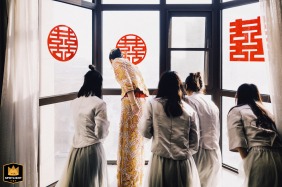 In Kaifeng, China, the bride and bridesmaids look down through a window, anticipating the groom's arrival. The scene captures a moment of excited waiting.